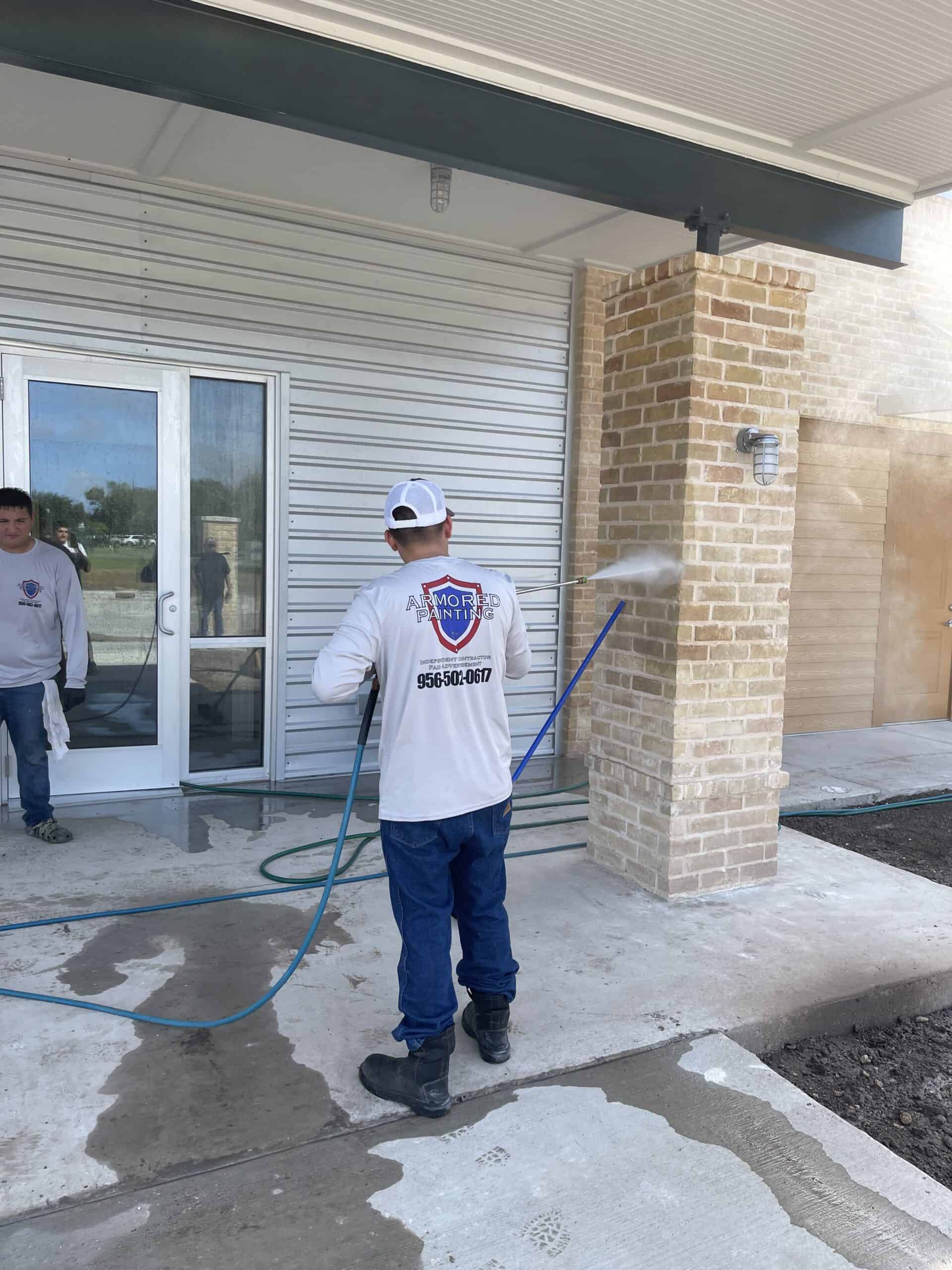 Crew member pressure washing a brick exterior wall